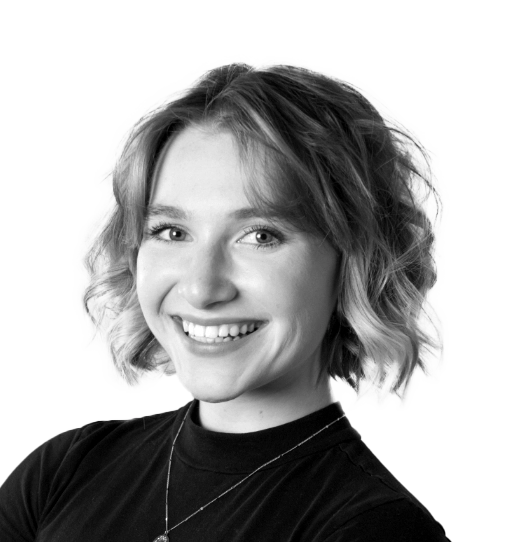 A black and white portrait captures a person with wavy, shoulder-length hair and a GRIN, wearing a dark top and necklace.