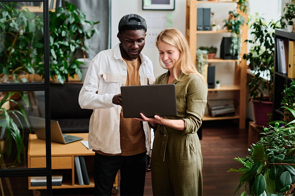 Two people talking influencer negotiation over a laptop in an office full of plants